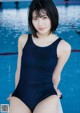 A woman in a blue bathing suit sitting on the edge of a pool.