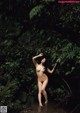 A naked woman standing in the middle of a forest.