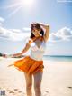 A woman in a white top and orange skirt on a beach.